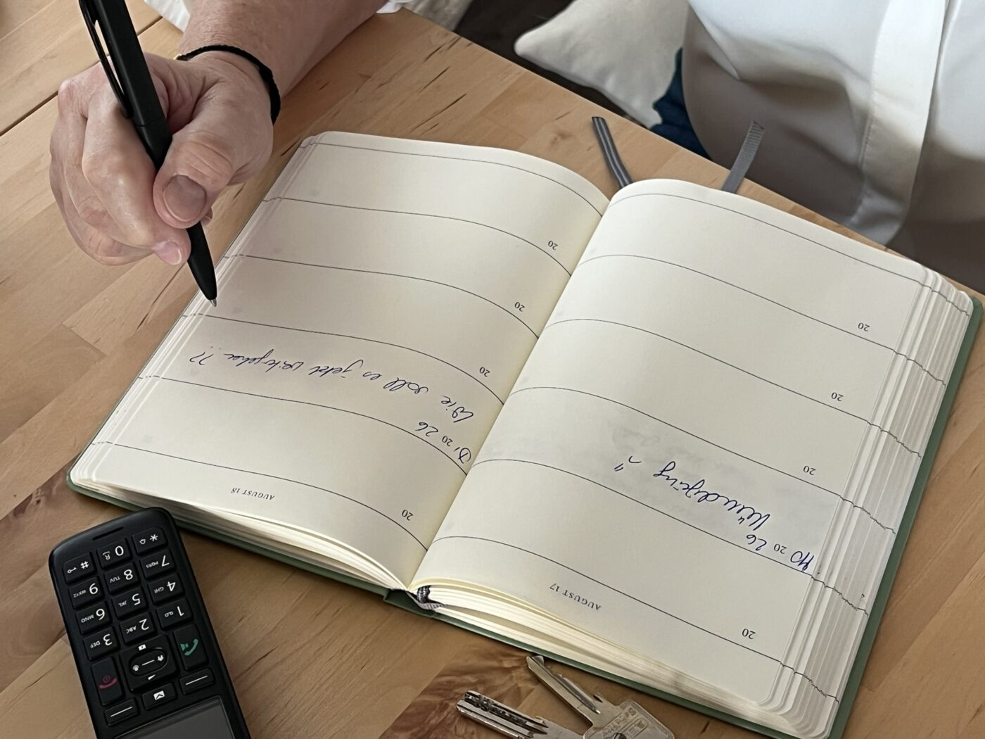 Eine Hand schreibt eine Notiz in einen aufgeschlagenen Kalender auf einem Holztisch