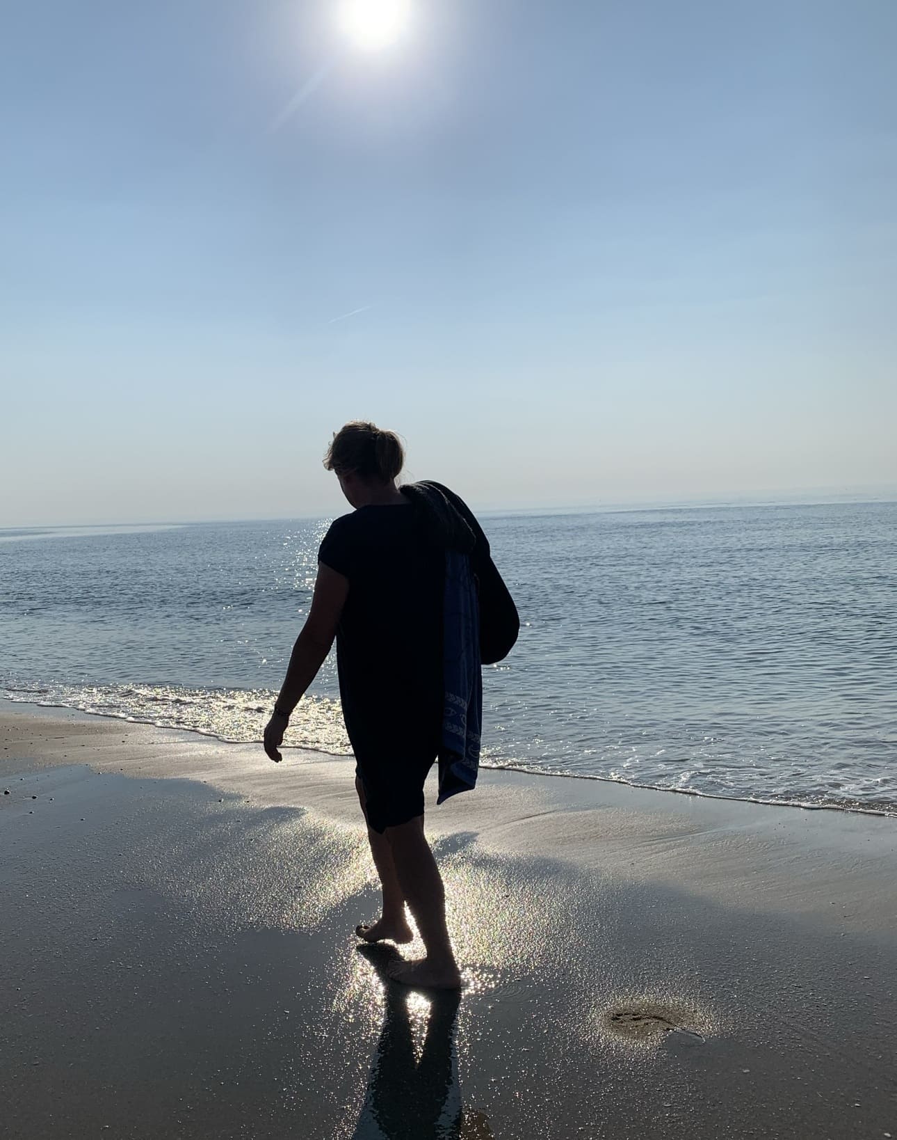 Eine Frau geht bei Gegenlicht am Spülsaum eines Strandes entlang