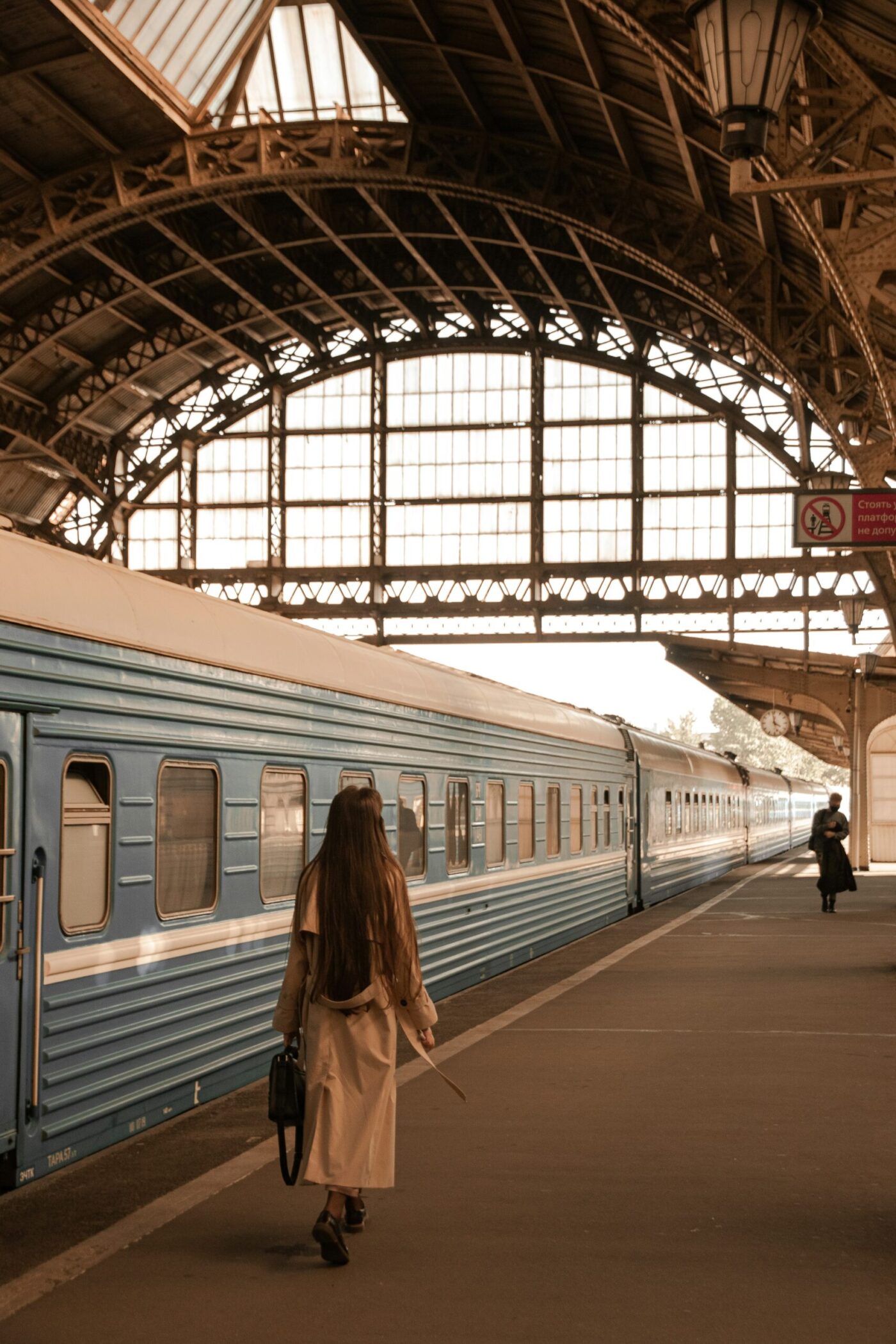 Eine Frau im hellen Mantel geht auf einem Bahnsteig an einem Zug entlang